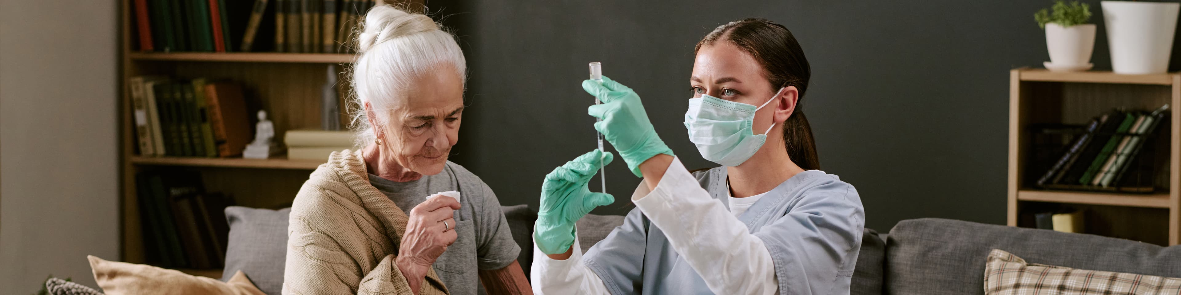 A nurse carefully preparing care at home beside an older woman
