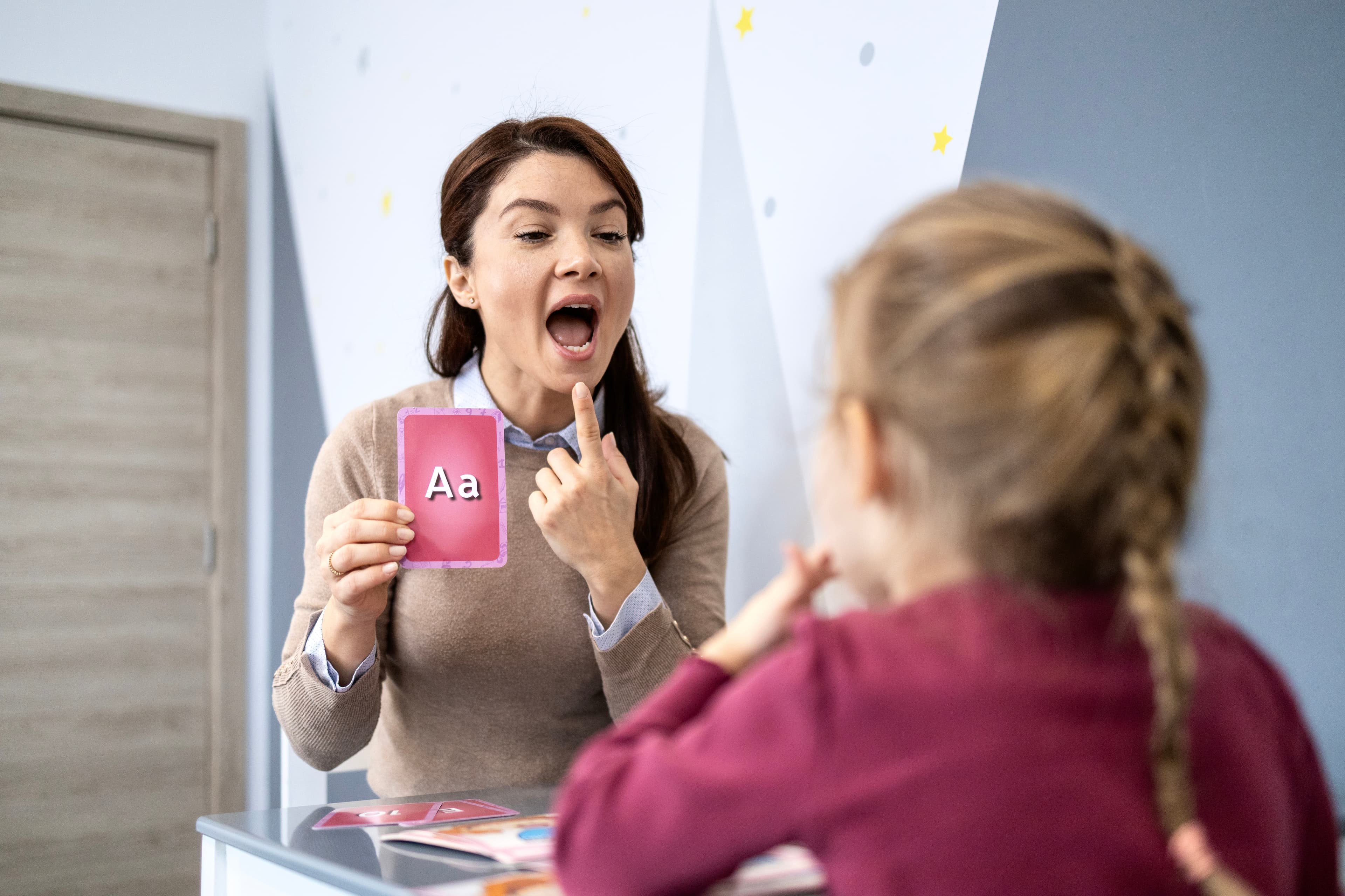 A speech therapist holding an Aa flashcard during a session with a child