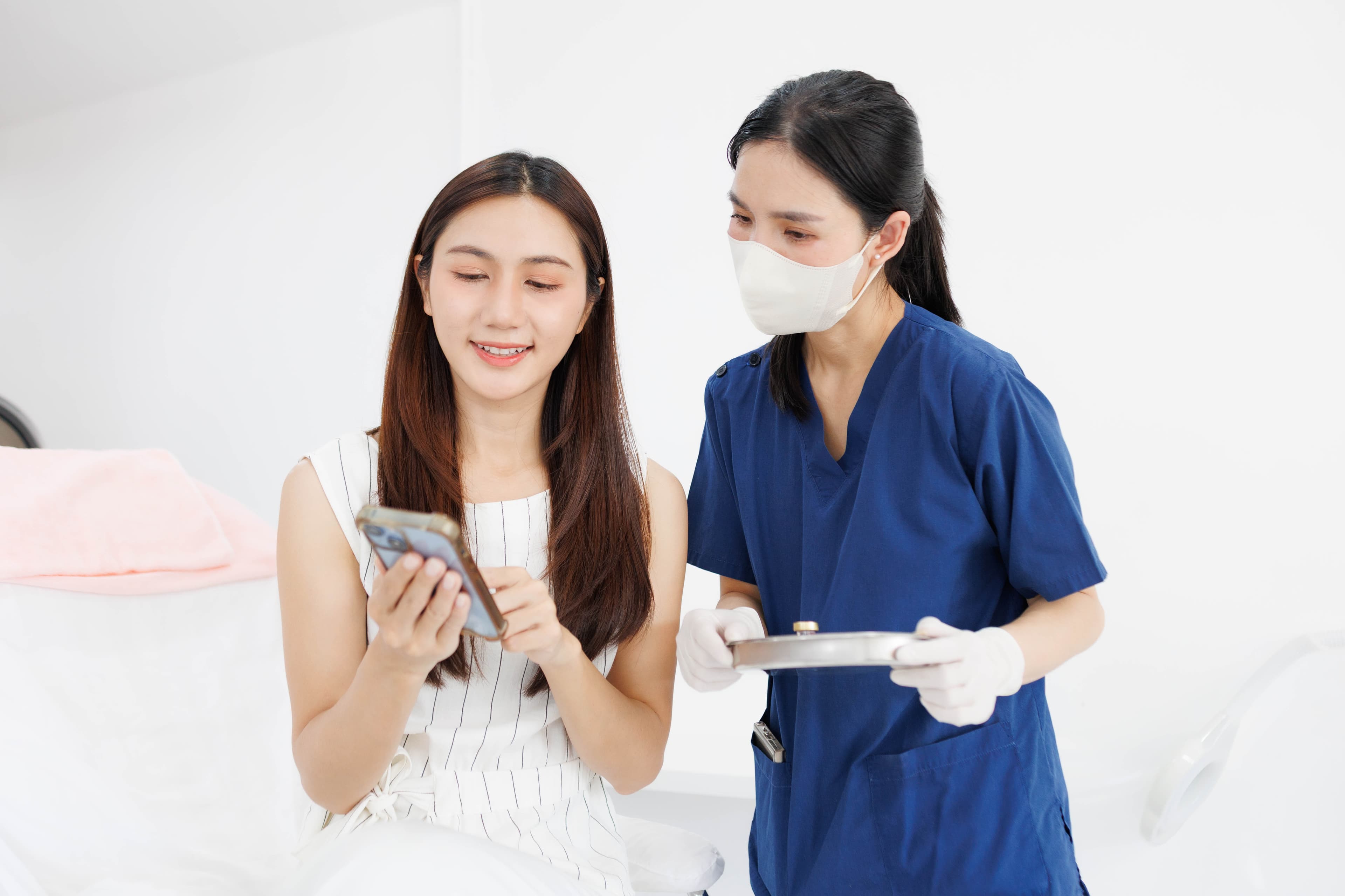 A masked nurse showing a patient a phone and a tablet during care
