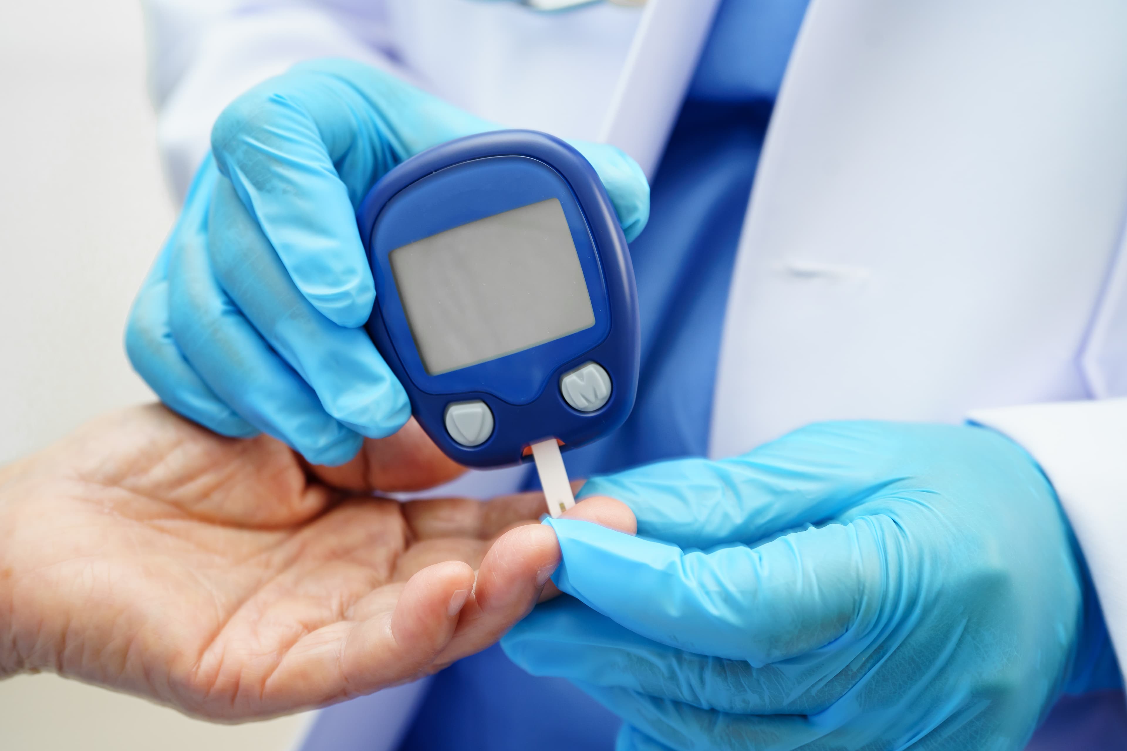A clinician in blue gloves holding a glucose meter with a test strip to an older person's fingertip