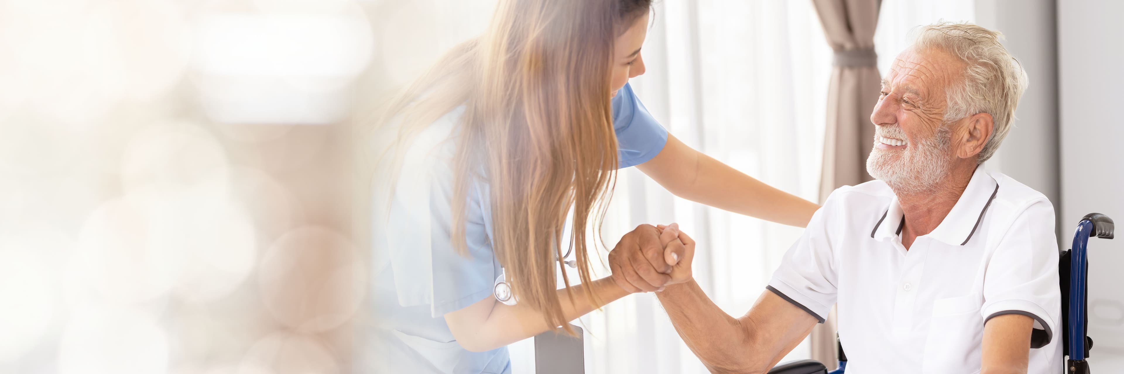 A nurse holding hands with a person seated in a wheelchair