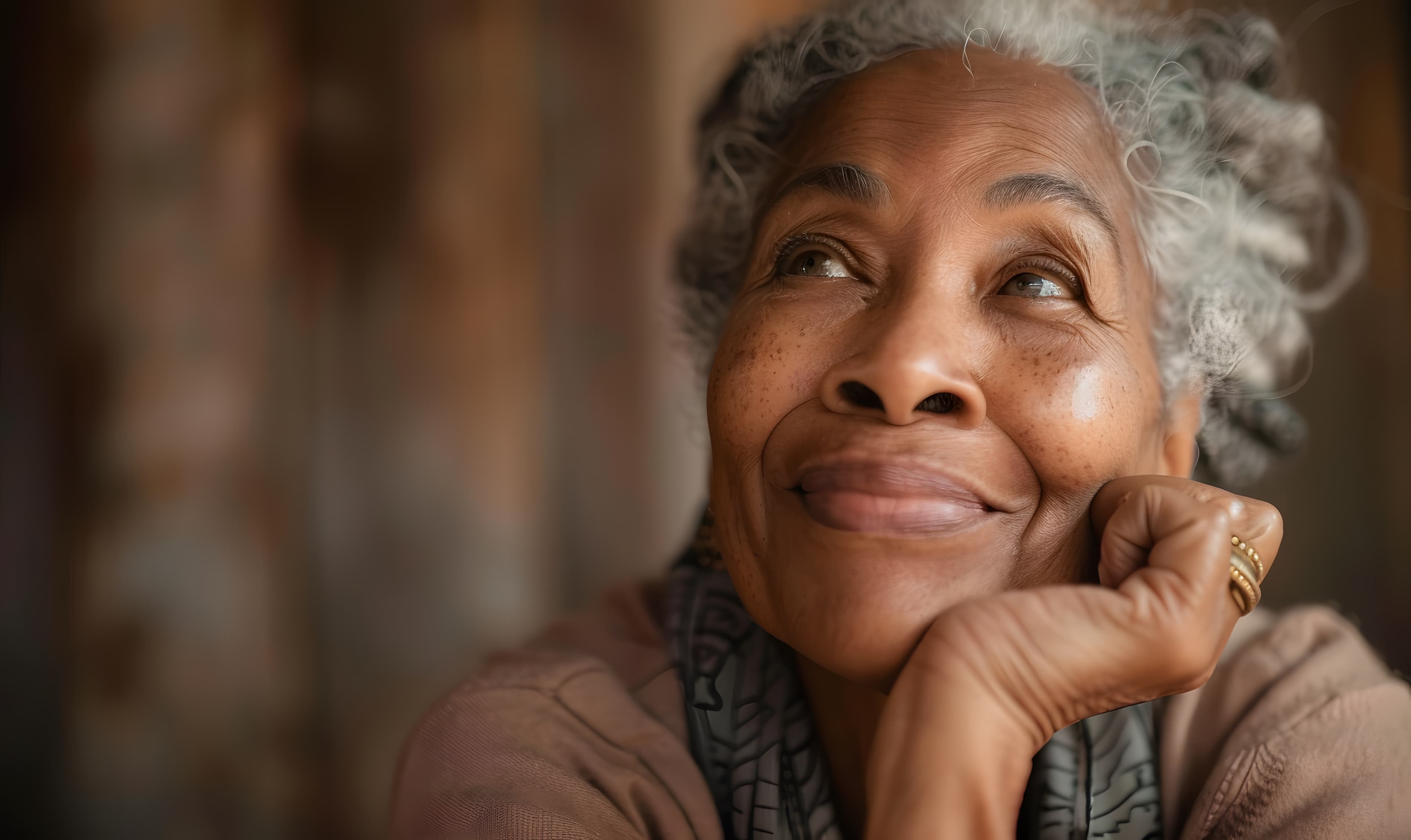 An older woman with gray hair resting her chin on one hand, smiling as she looks up